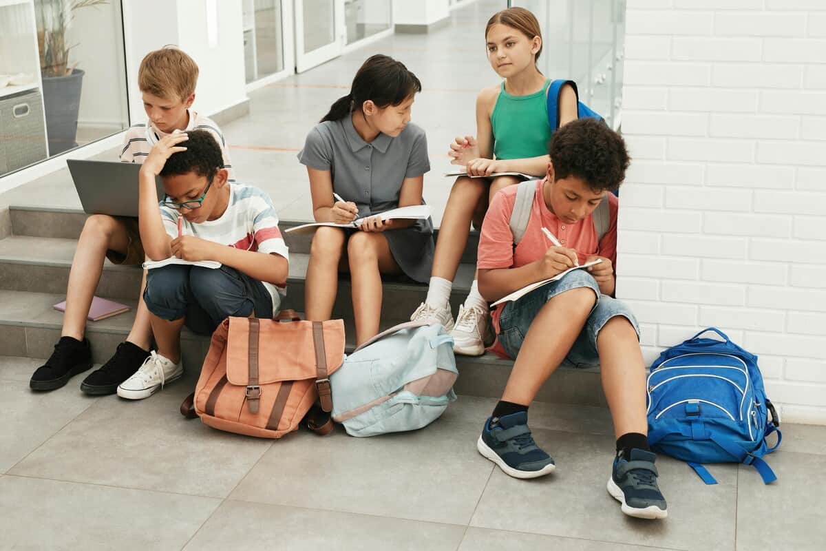 Bambini seduti sui gradini della scuola con gli zaini