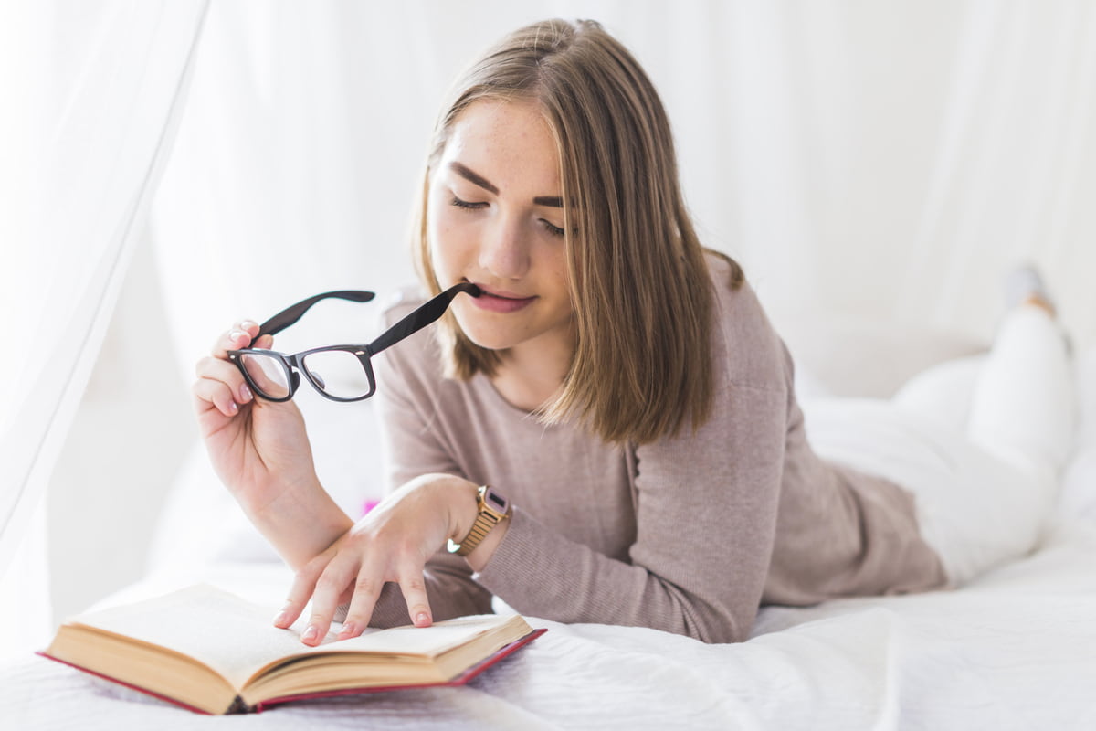 Ragazza che legge un libro tenendo in mano gli occhiali