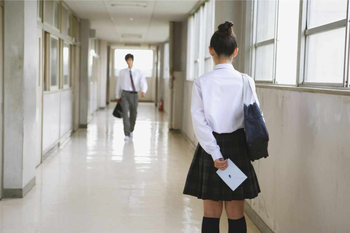 Ragazza in uniforme nel corridoio di una scuola che nasconde una lettera