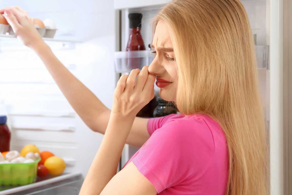 Donna bionda che si tappa il naso con frigorifero aperto
